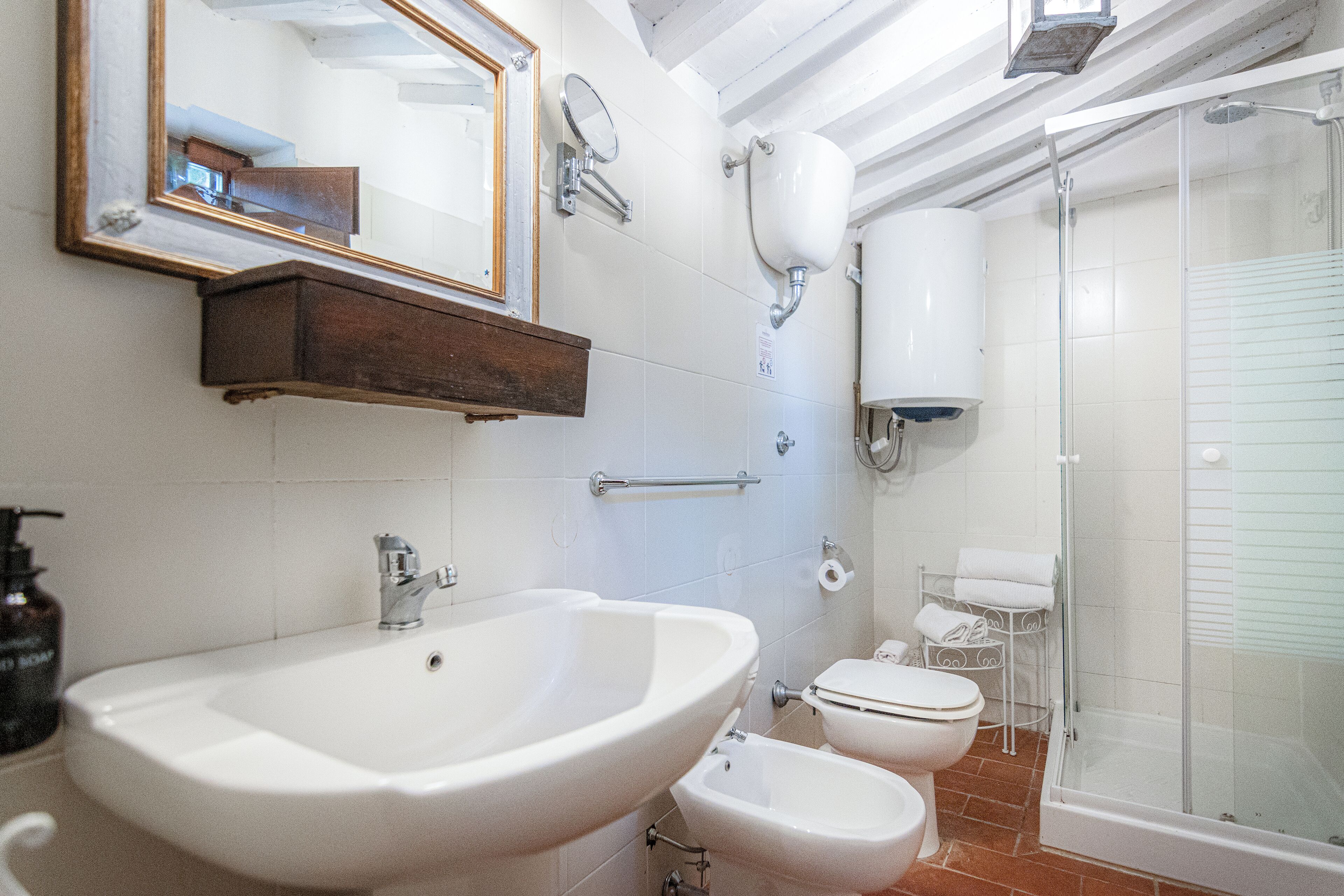 Un baño con un lavamanos grande, dos inodoros, una ducha, un espejo y un dispensador de jabón.