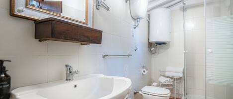 Un baño con un lavamanos grande, dos inodoros, una ducha, un espejo y un dispensador de jabón.