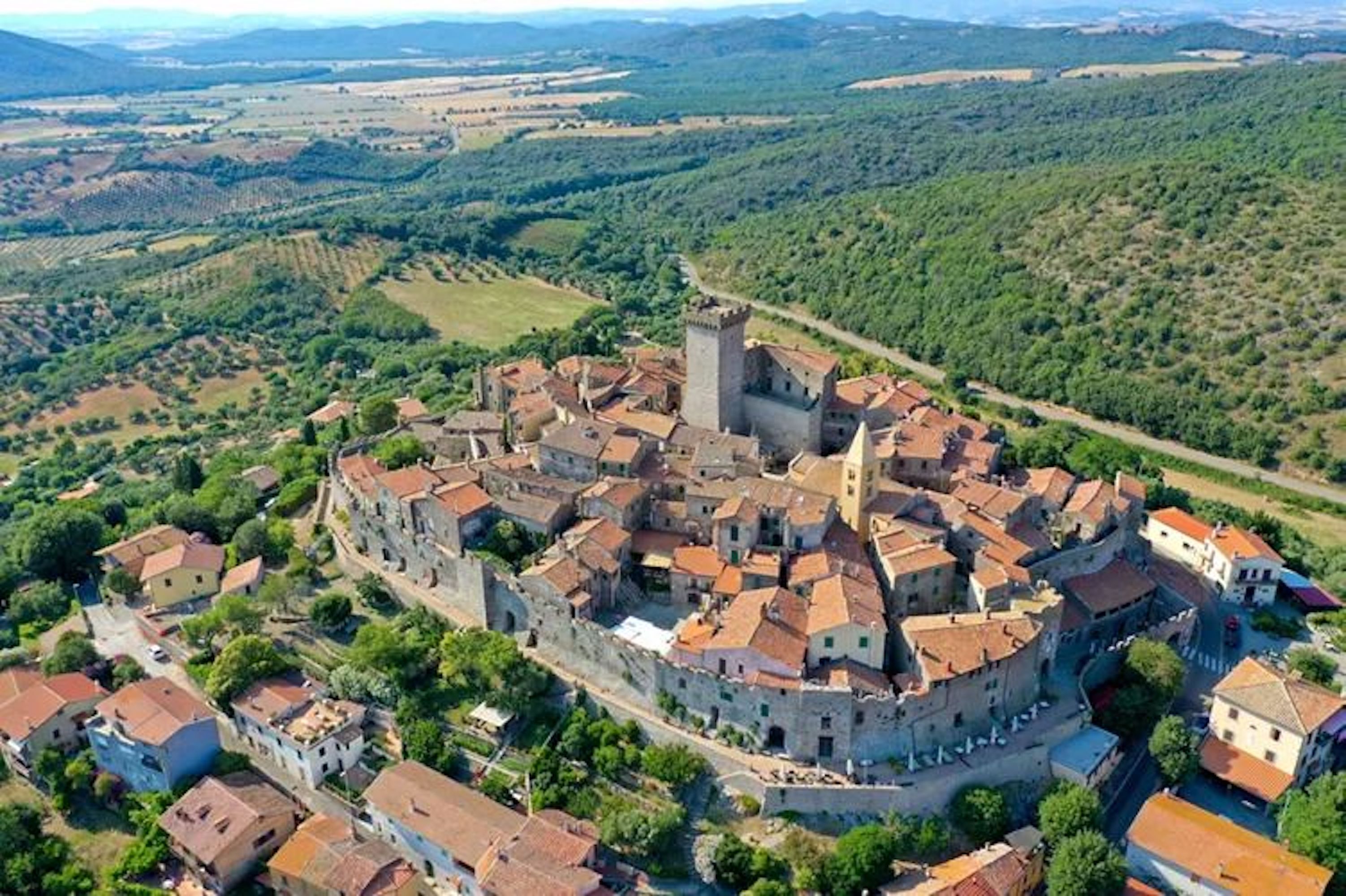 An aerial view of a historic town with a central castle, surrounded by traditional buildings and lush greenery.