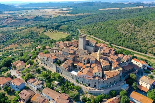 Vista aérea de un pueblo histórico con un castillo central, rodeado de edificios tradicionales y abundante vegetación.