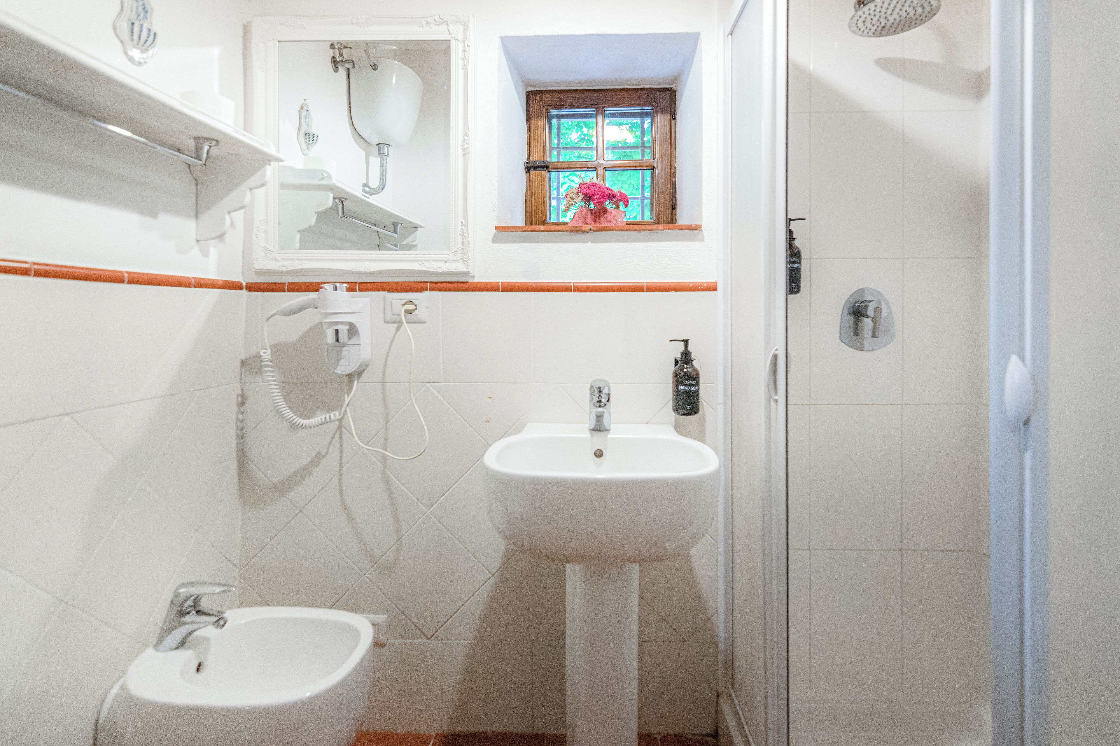Ein Badezimmer mit einem Bidet, einem Waschbecken und einem Fenster mit Blick ins Grüne.