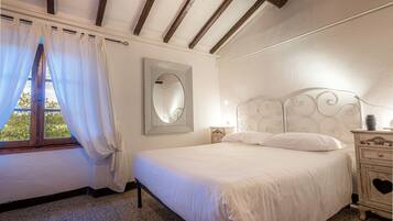 A bedroom with a bed, a nightstand, a mirror, and a window with curtains.
