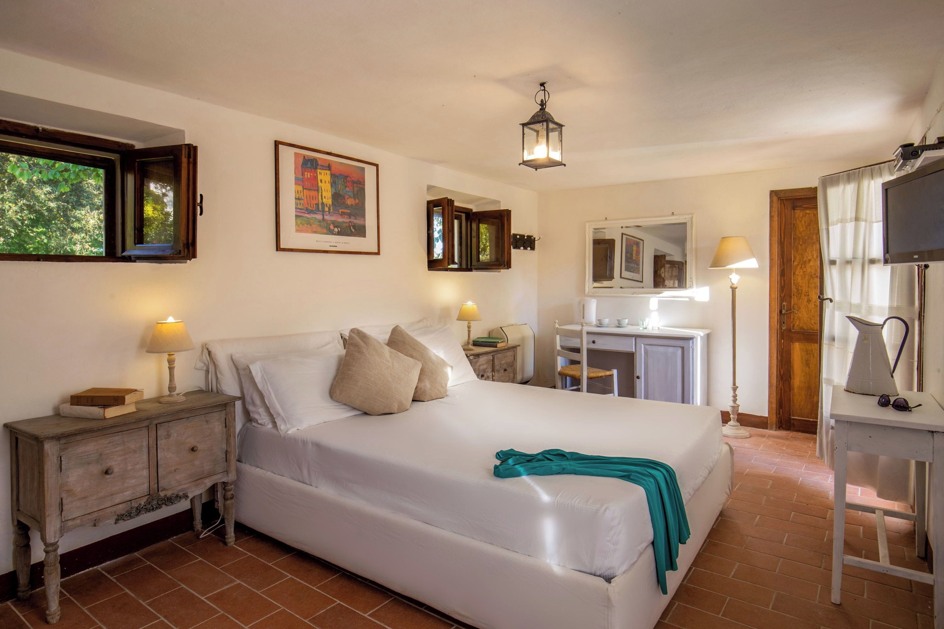 A bedroom with a bed, bedside tables, a mirror, a TV, and a window with curtains.