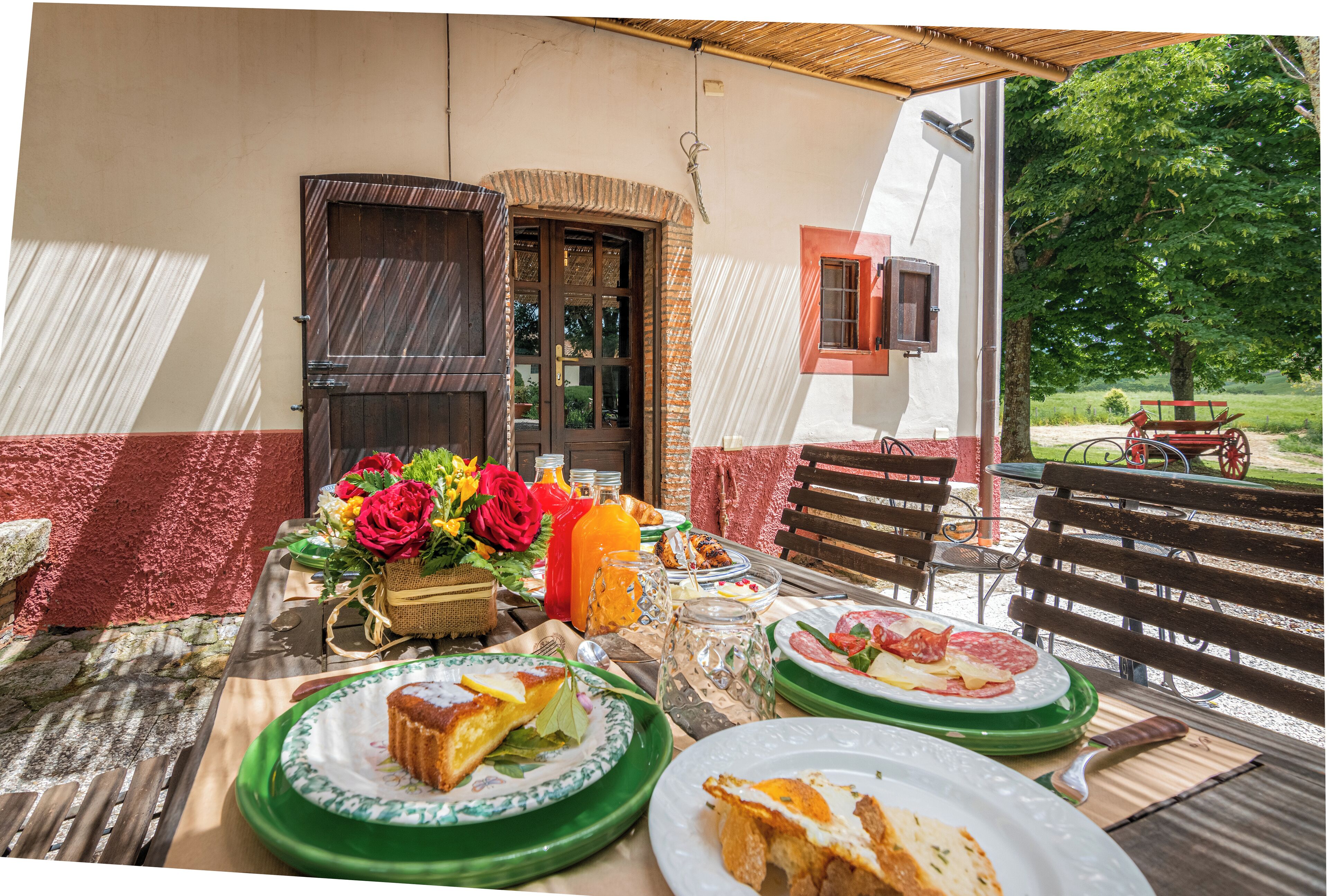 An outdoor dining area with a table set for two, featuring plates of food, a vase of flowers, and a wooden bench.