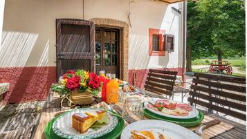 Een terras met eethoek, een tafel gedekt voor twee personen, borden met eten, een bloevas en een houten bank.