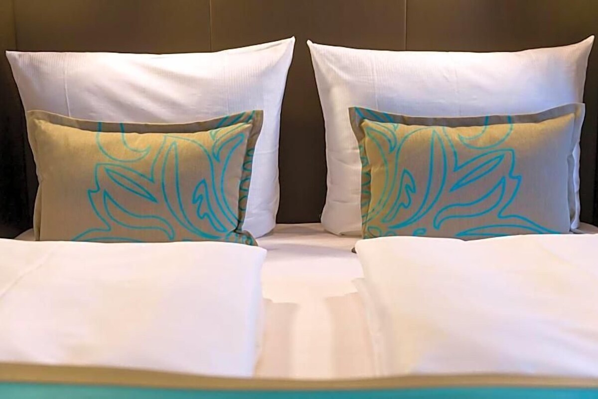 Ein Bett mit weißer Bettwäsche und zwei Kissen mit Blätermotiv.
