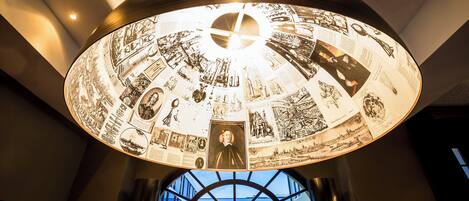 Techo circular con ilustraciones y textos históricos, entrada moderna de un edificio con puertas de vidrio, y una vista del cielo a través de las ventanas.
