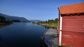 Un edificio rojo con un muelle que se adentra en aguas tranquilas, rodeado de vegetación y montañas.