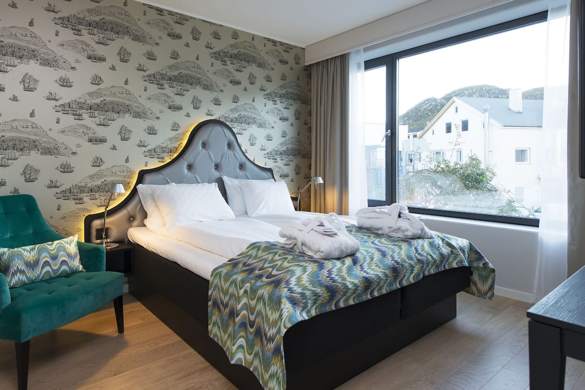 Quarto de hotel com uma cama grande, uma poltrona verde e vista para edifícios pela janela.