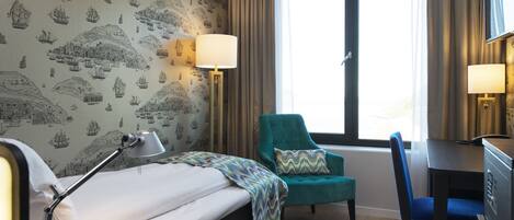 A hotel room with a bed, a desk, a chair, and a window with curtains.