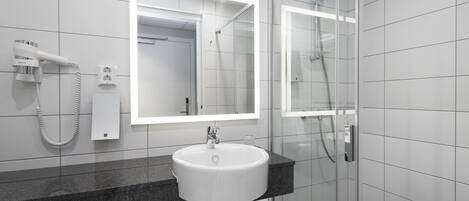 A modern bathroom with a white sink, a glass shower enclosure, and a hairdryer on the wall.