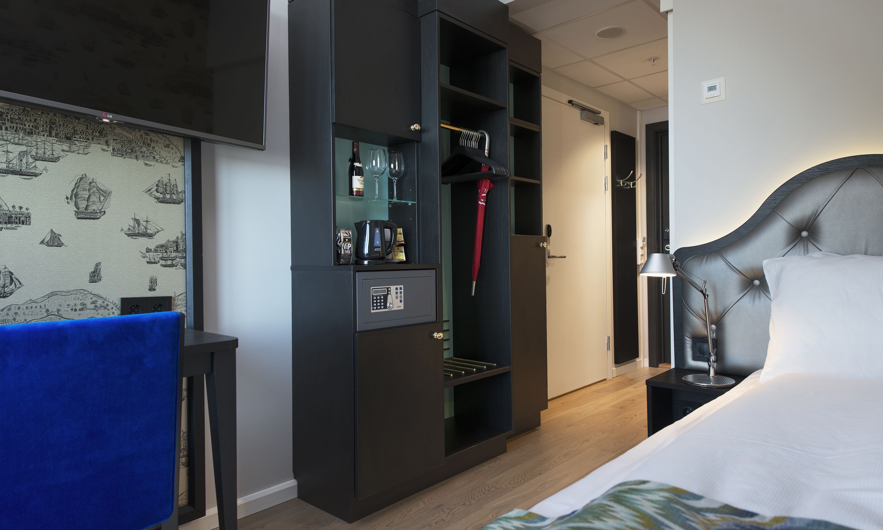 Ein Hotelzimmer mit Bett, Kleiderschrank, Schreibtisch und einer Wand mit nautisch gestalteter Tapete.