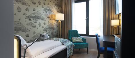 A hotel room with a bed, a desk, a chair, and a window with curtains.