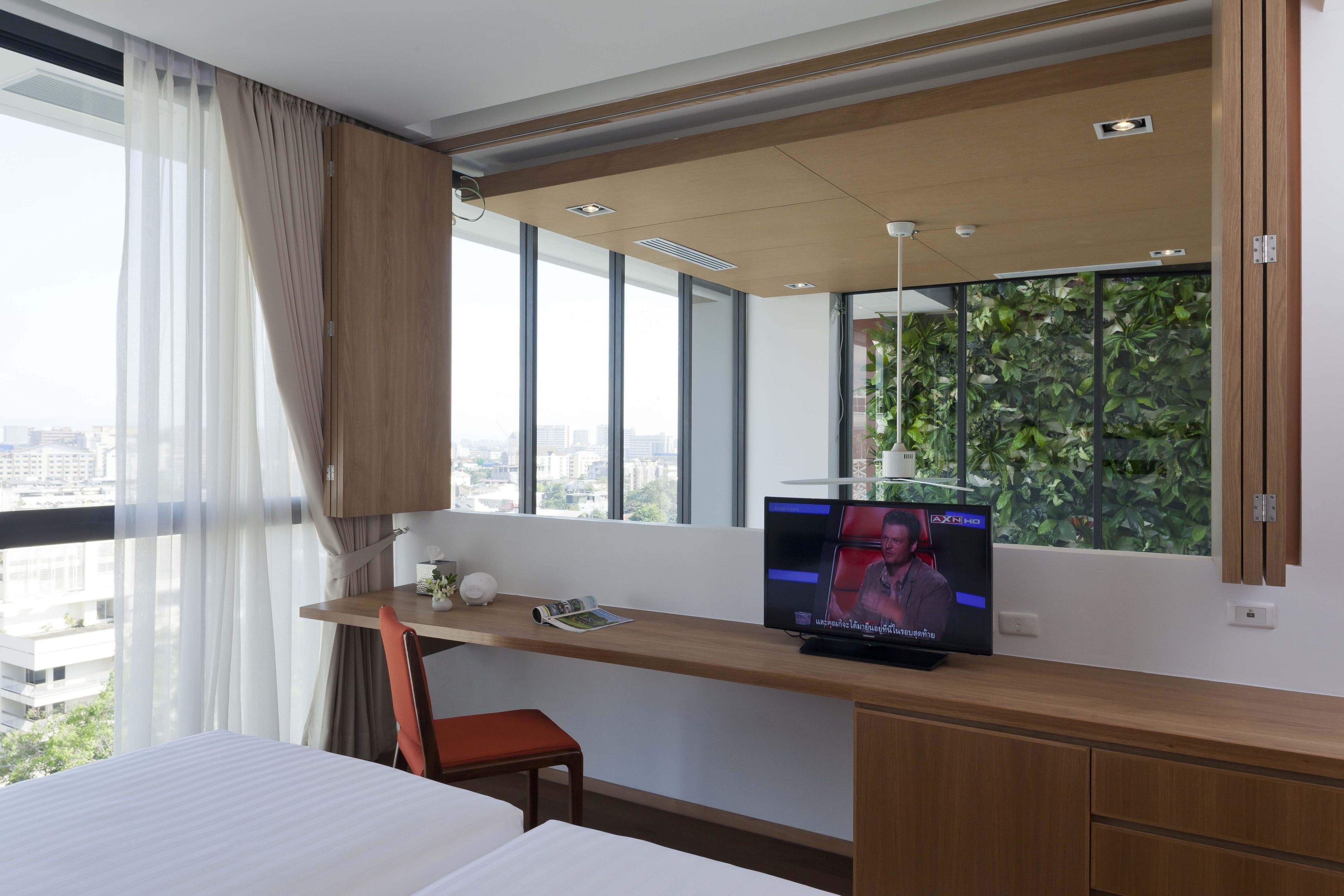 A hotel room with a bed, a desk with a TV, a chair, and a window with a city view.