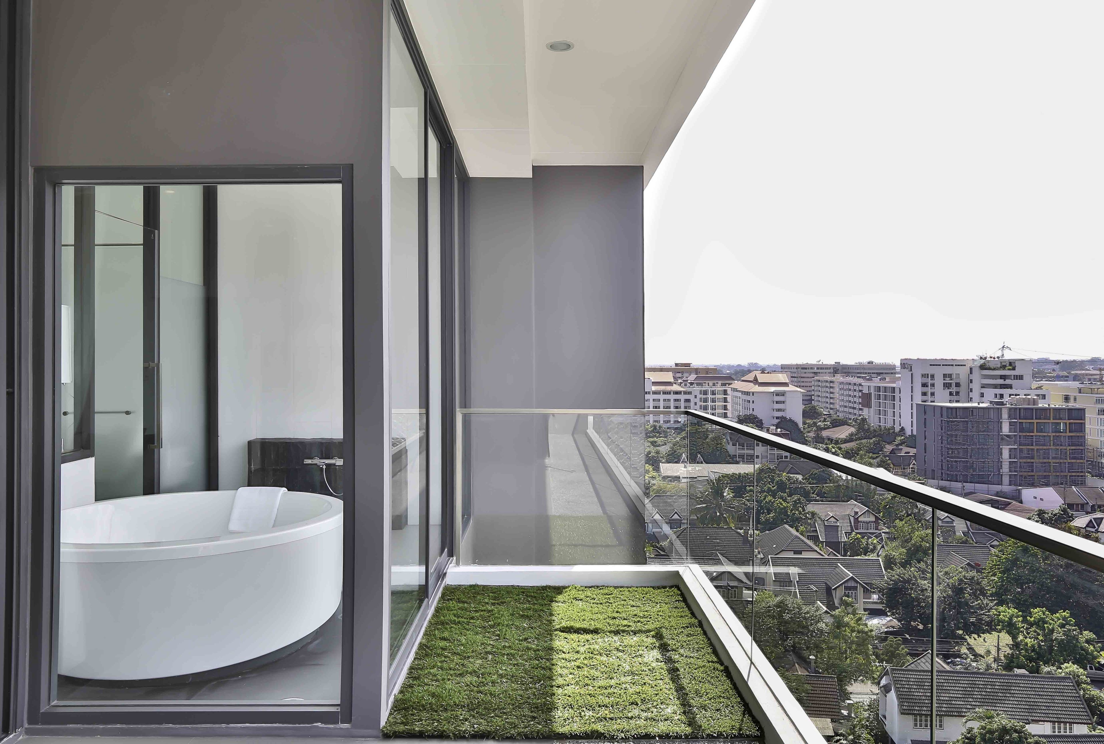 A modern bathroom with a large bathtub and a balcony with a green artificial grass area.