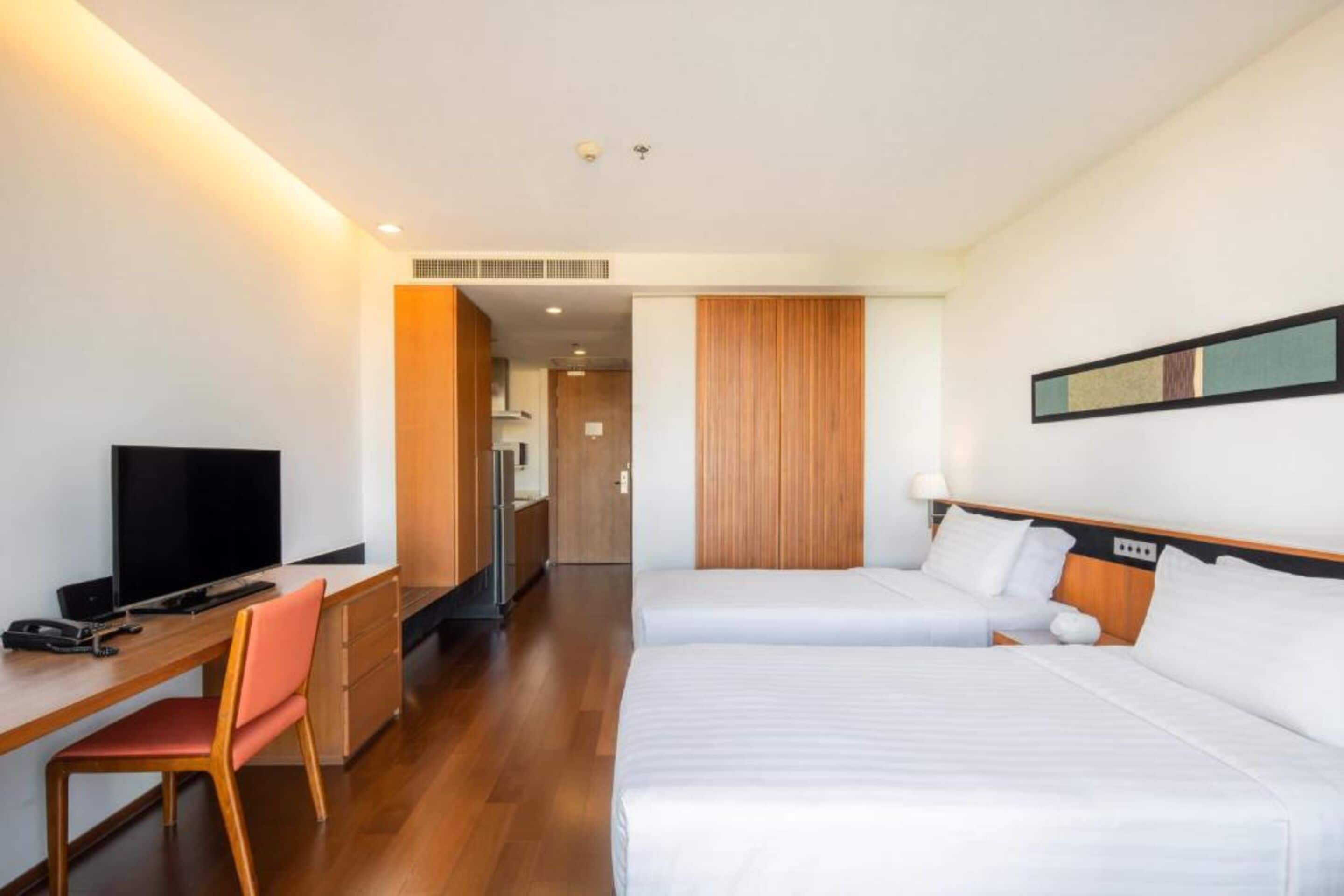 Una habitación de hotel con un escritorio de madera, televisor, dos camas y un espejo en la pared.