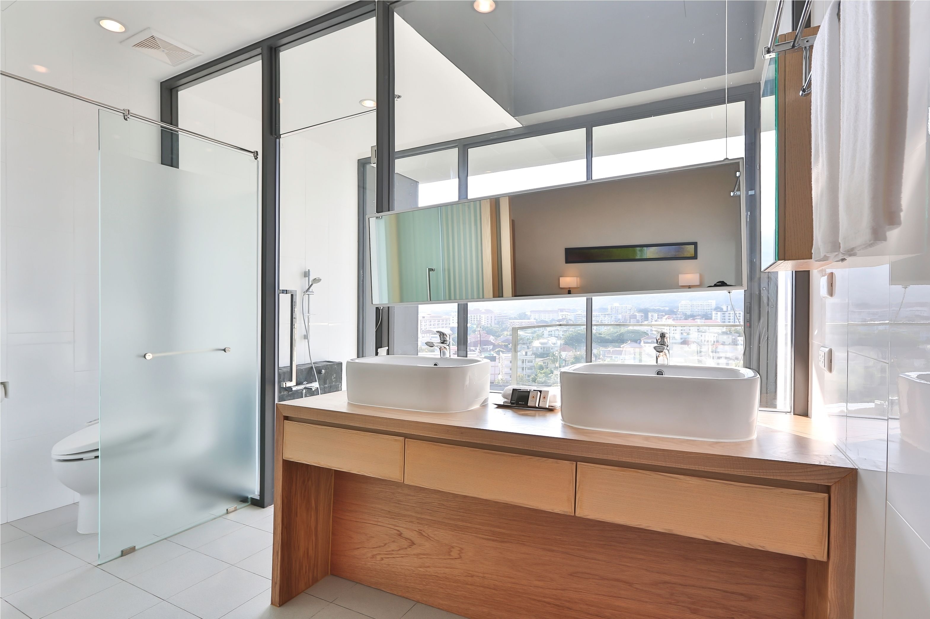 A modern bathroom with two large white sinks, a glass shower enclosure, and a large mirror reflecting a city view.