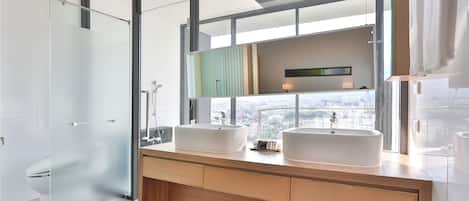 A modern bathroom with two large white sinks, a glass shower enclosure, and a large mirror reflecting a city view.