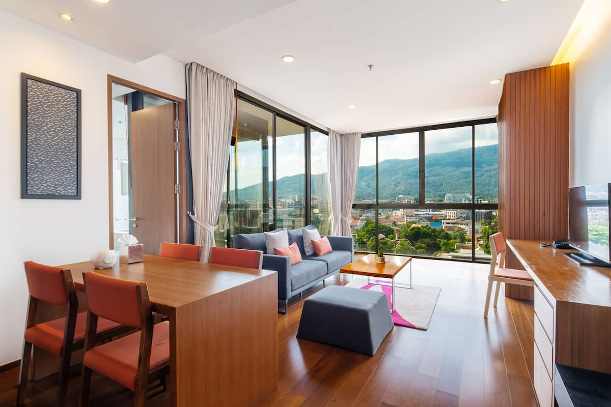 A modern living room with a dining area, large windows with a city and mountain view, and a kitchen area.
