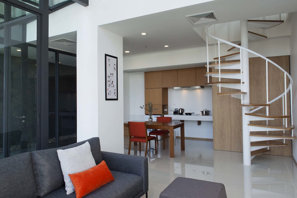 A modern interior with a living area featuring a sofa and a dining table, a kitchen with wooden cabinets, and a spiral staircase.