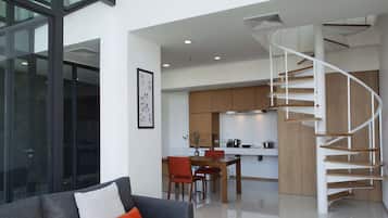 A modern interior with a living area featuring a sofa and a dining table, a kitchen with wooden cabinets, and a spiral staircase.