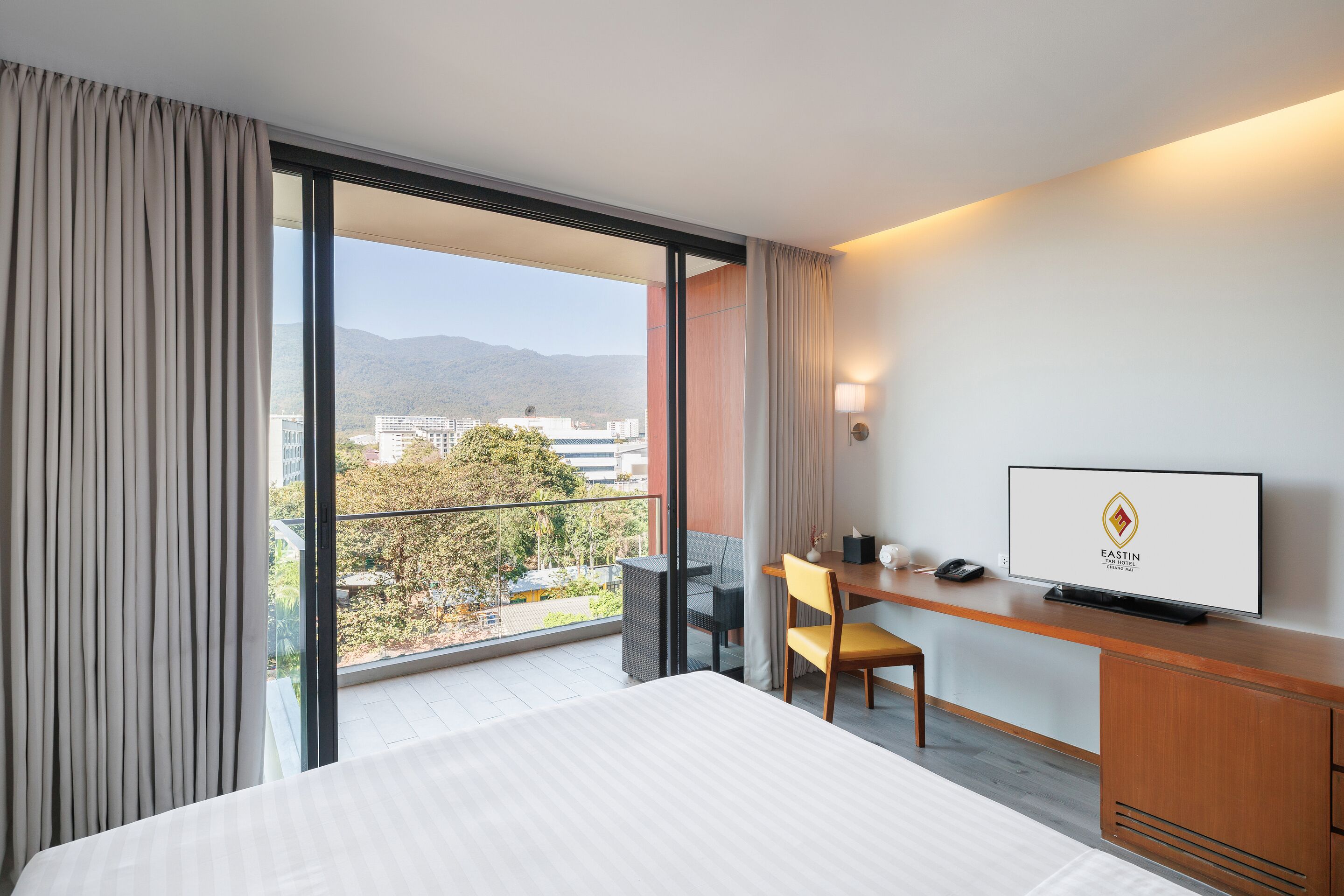 Une chambre d’hôtel comprenant un lit, un bureau avec une chaise, une télévision et une vue sur la ville et les montagnes.