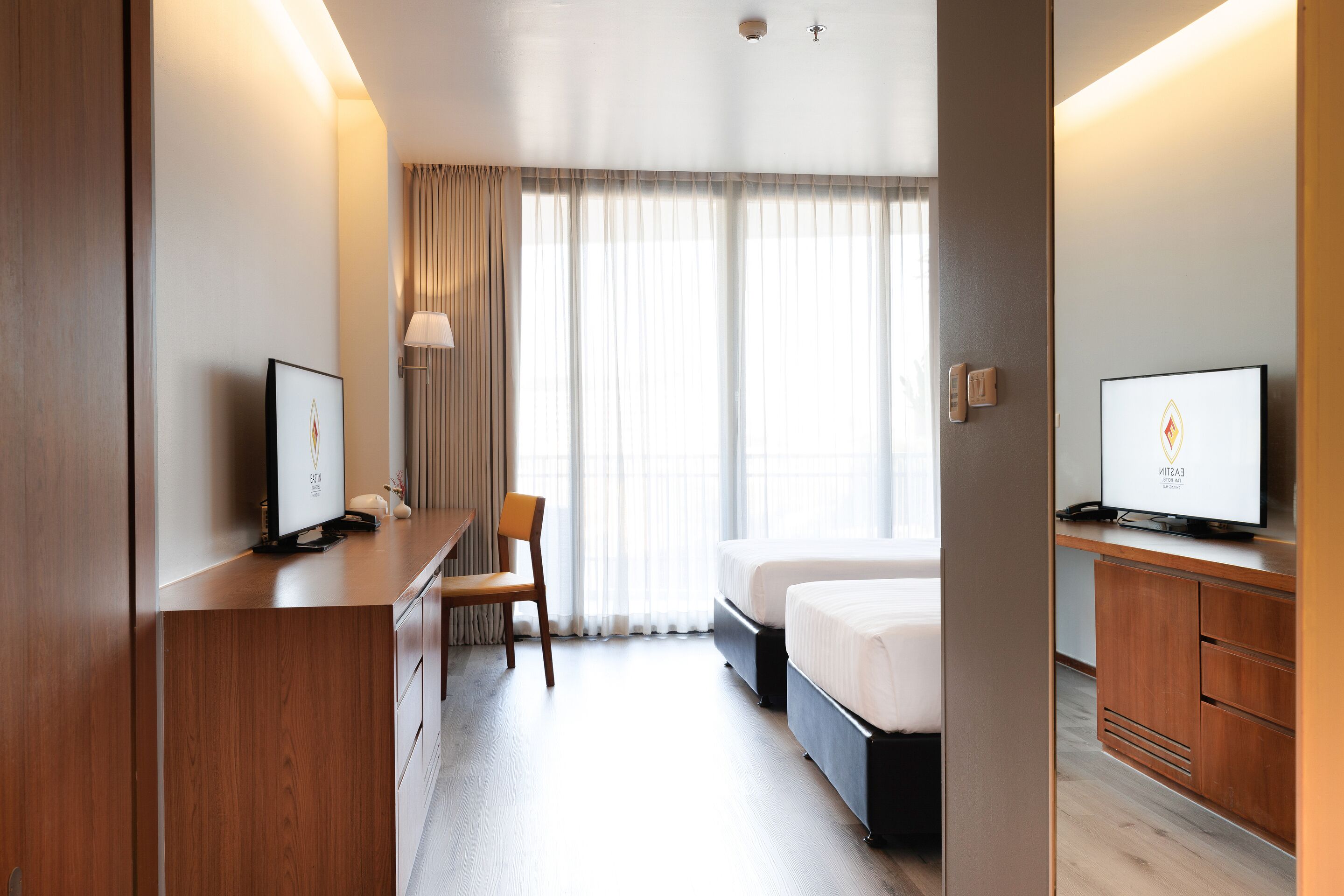 A hotel room with a bed, a desk, a chair, a television, and a window with curtains.
