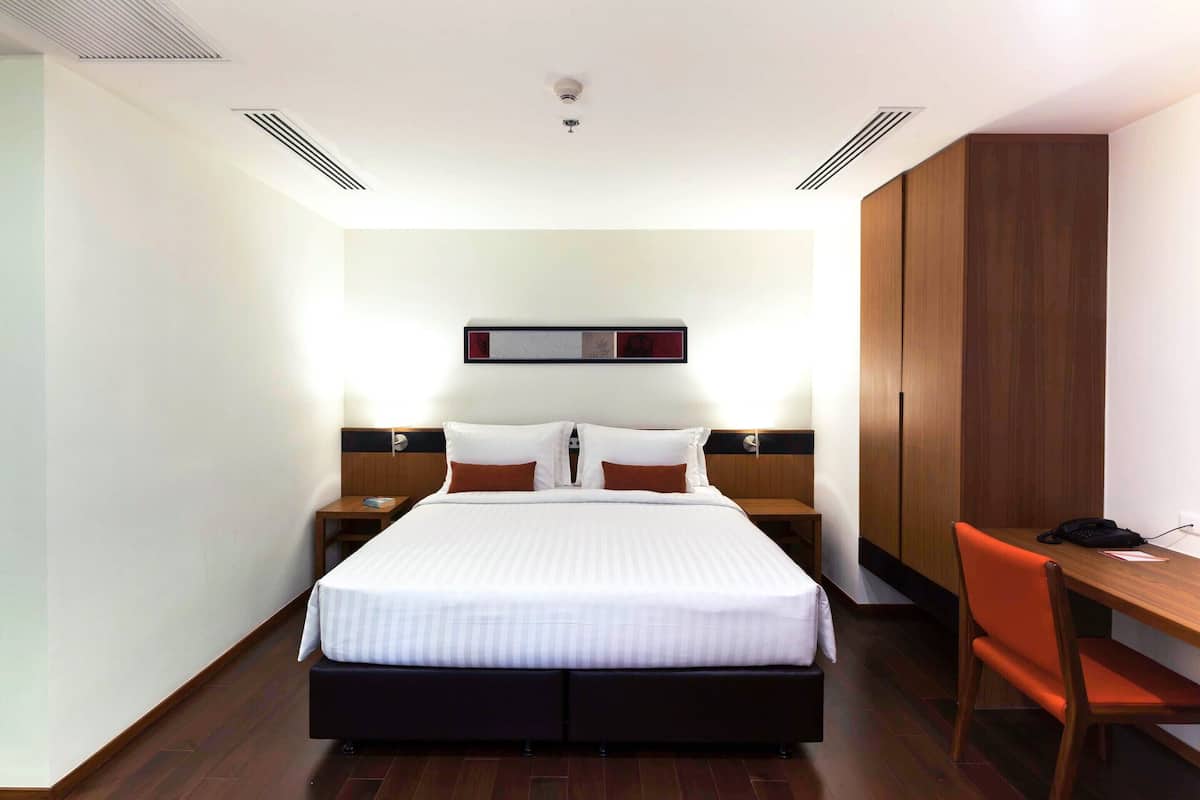 A hotel room with a large bed, two bedside tables, a desk, and a wardrobe.