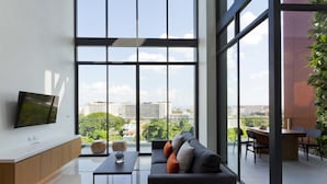 Una sala de estar moderna con un ventanal grande, un televisor de pantalla plana, un sofá y una zona de comedor con sillas y una mesa.