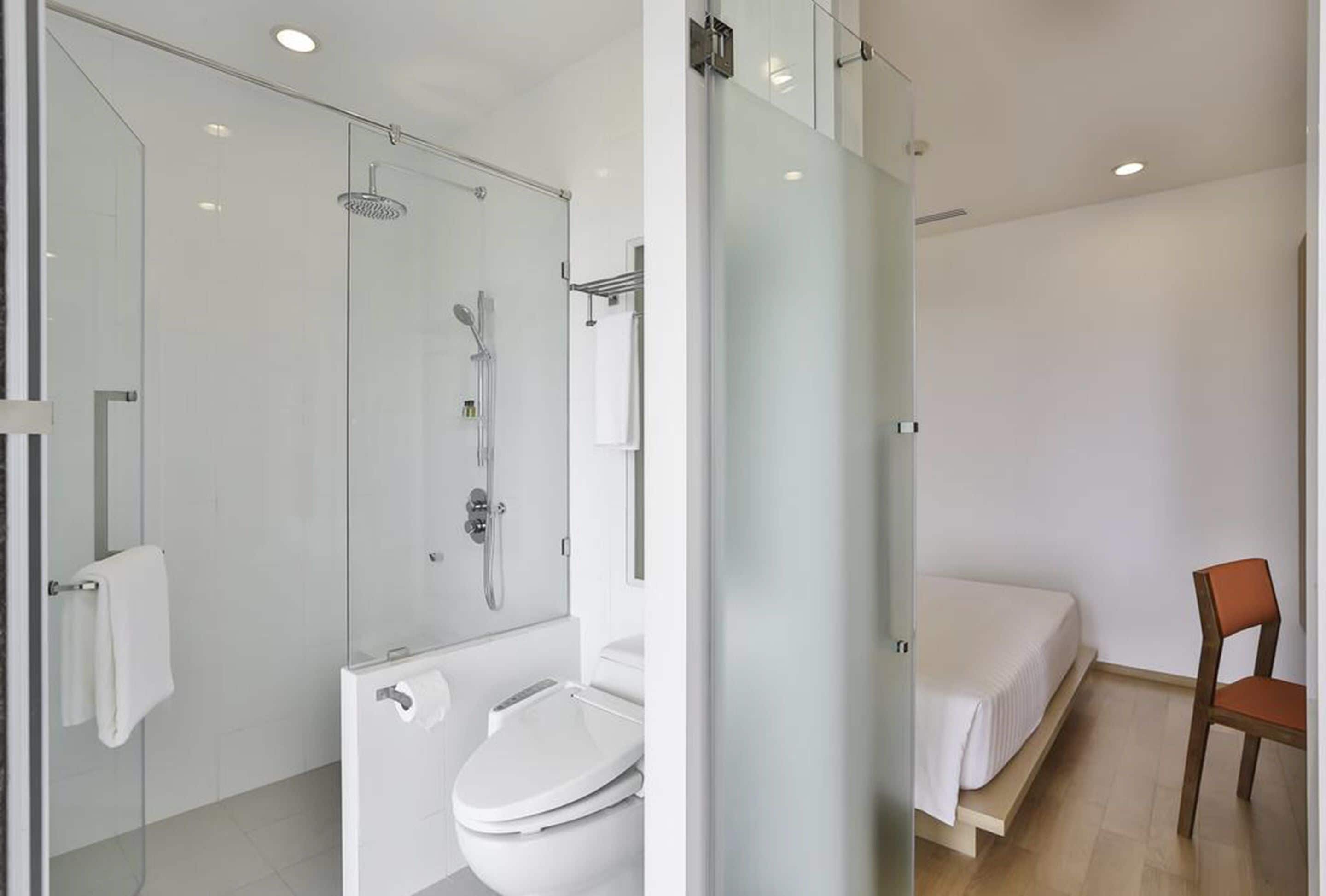 Un baño moderno con cabina de ducha de vidrio, un inodoro y una cama en la habitación contigua.