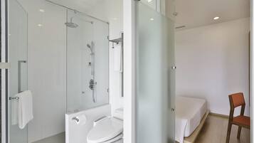 Un baño moderno con cabina de ducha de vidrio, un inodoro y una cama en la habitación contigua.