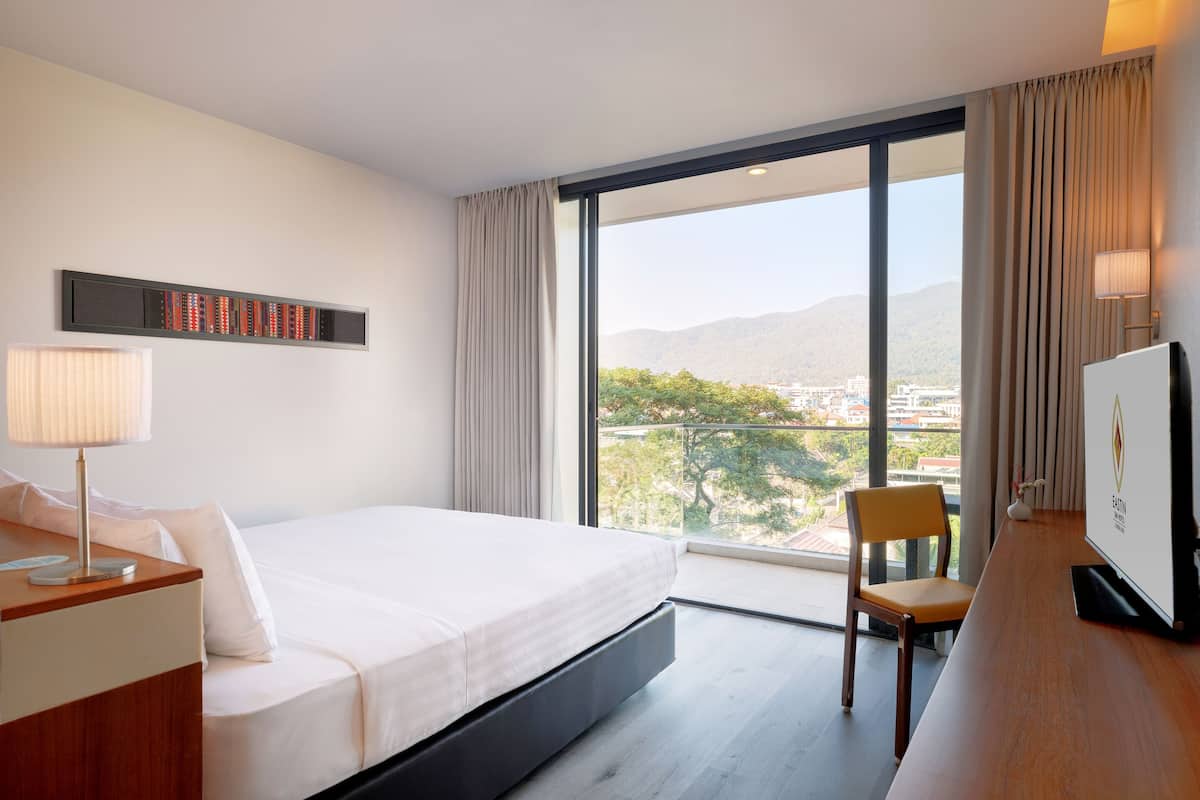 A hotel room with a large bed, a desk, a chair, a TV, and a window with a city view.
