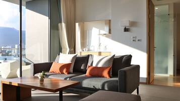 A modern living room with a grey sofa, orange cushions, a wooden coffee table, and a large window offering a city view.