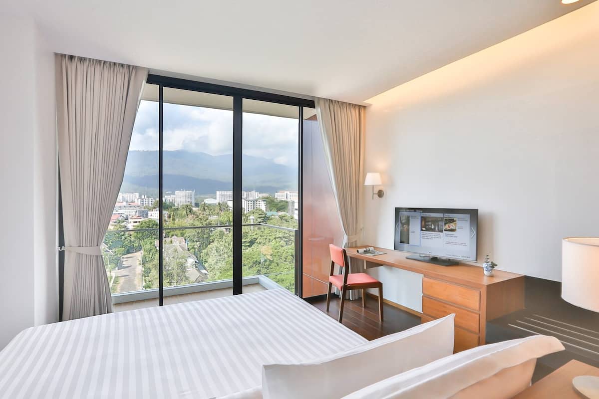 A hotel room with a bed, a desk with a computer, a chair, and a TV.