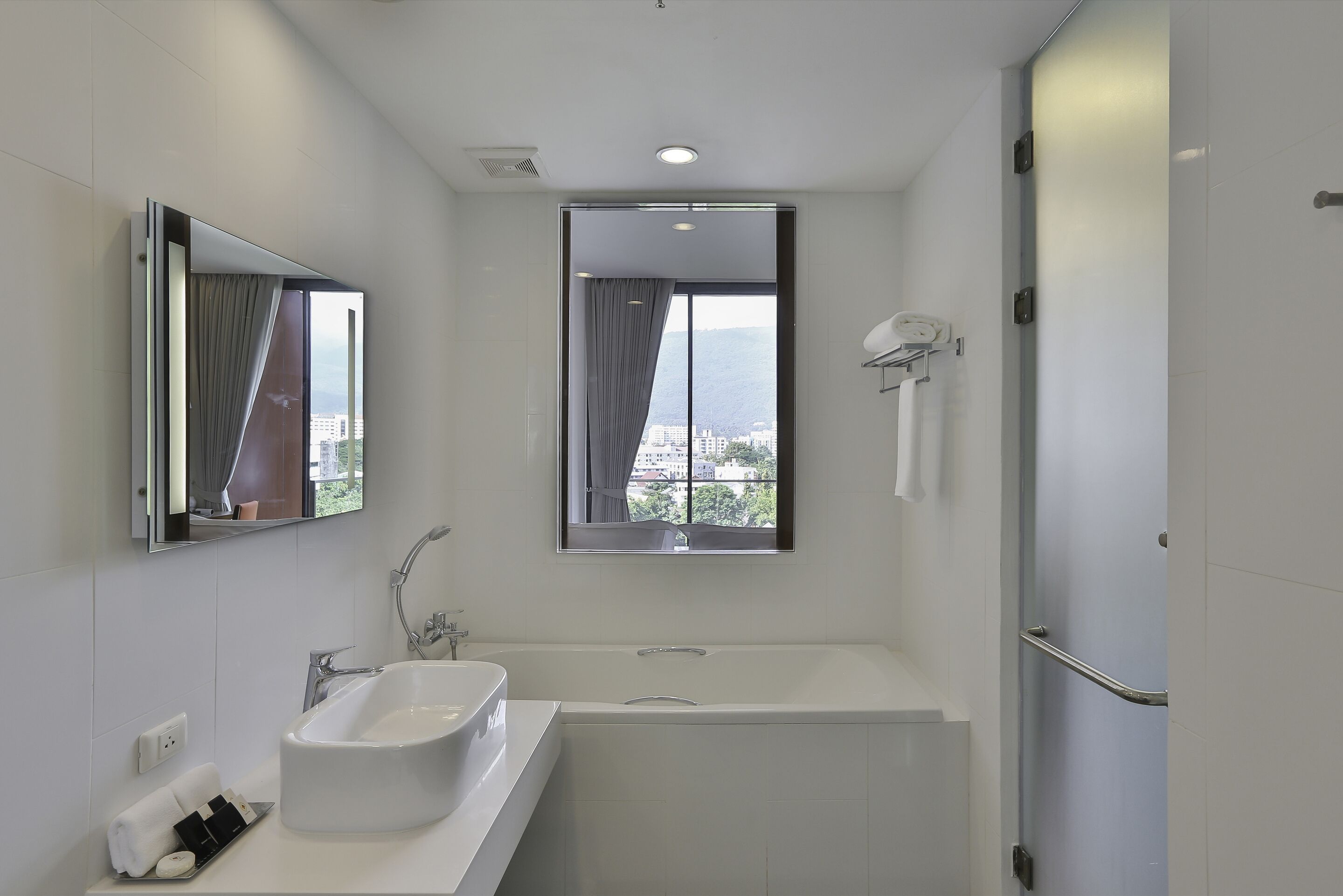 A modern bathroom with a bathtub, a large mirror, a window with a view, and a towel rack.