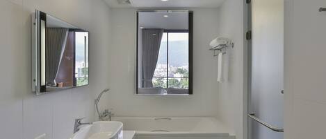 A modern bathroom with a bathtub, a large mirror, a window with a view, and a towel rack.
