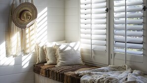 A cozy room with a built-in bench, a woven basket, and a view through white shutters. - White Water (Cambria)