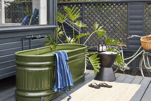 A green outdoor bathtub, a bicycle, and a black planter on a wooden deck.