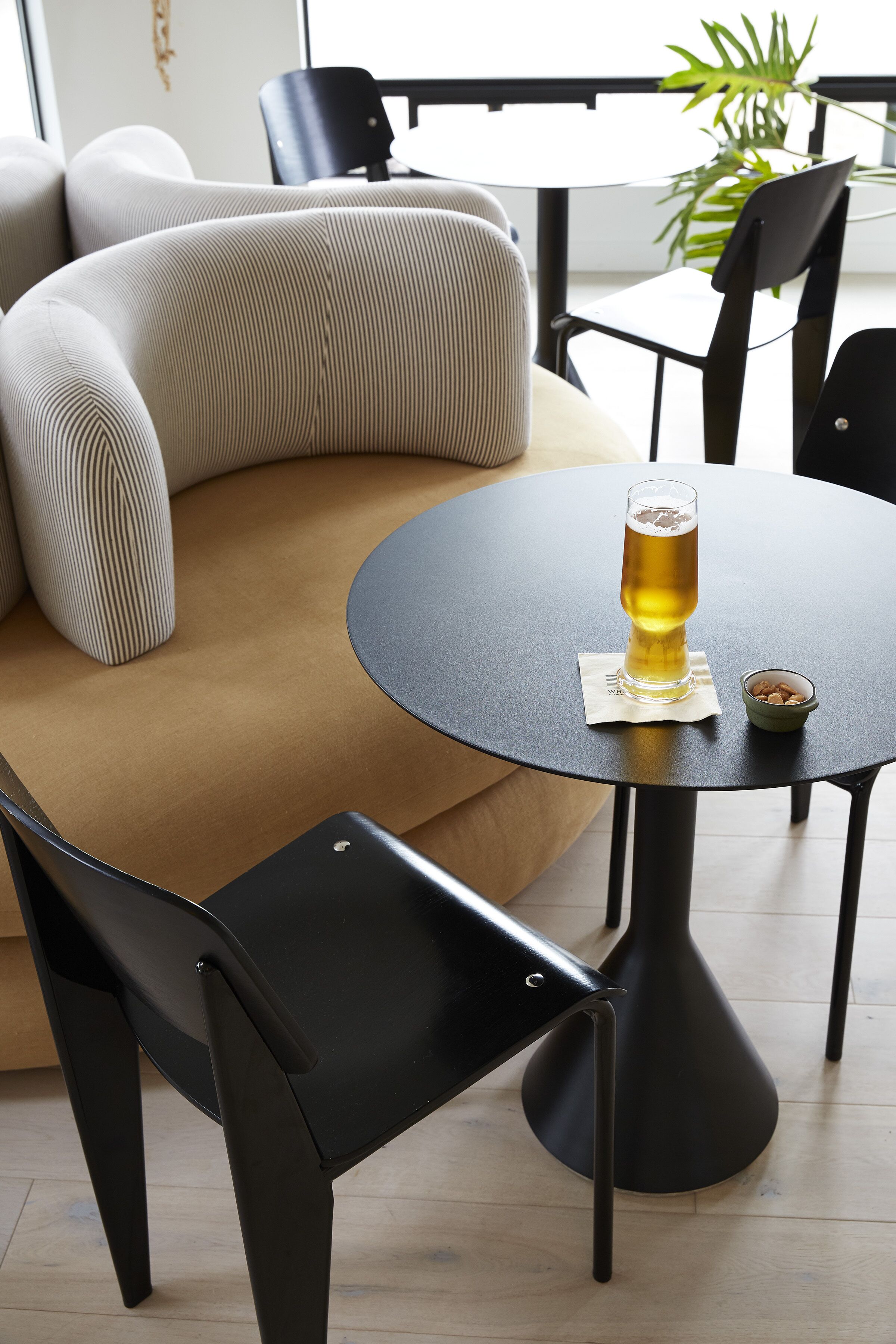A round table with a glass of beer, a bowl of nuts, and a black chair.