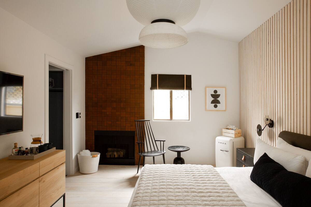 Ein Schlafzimmer mit Bett, Schminktisch, Stuhl, kleinem Tisch, Kamin und Fernseher.