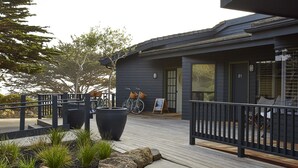 A modern building with a dark exterior, a wooden deck, and a metal railing. - White Water (Cambria)