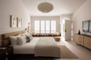 A modern bedroom with a large bed, a bench, a television, and a view of the outdoors.