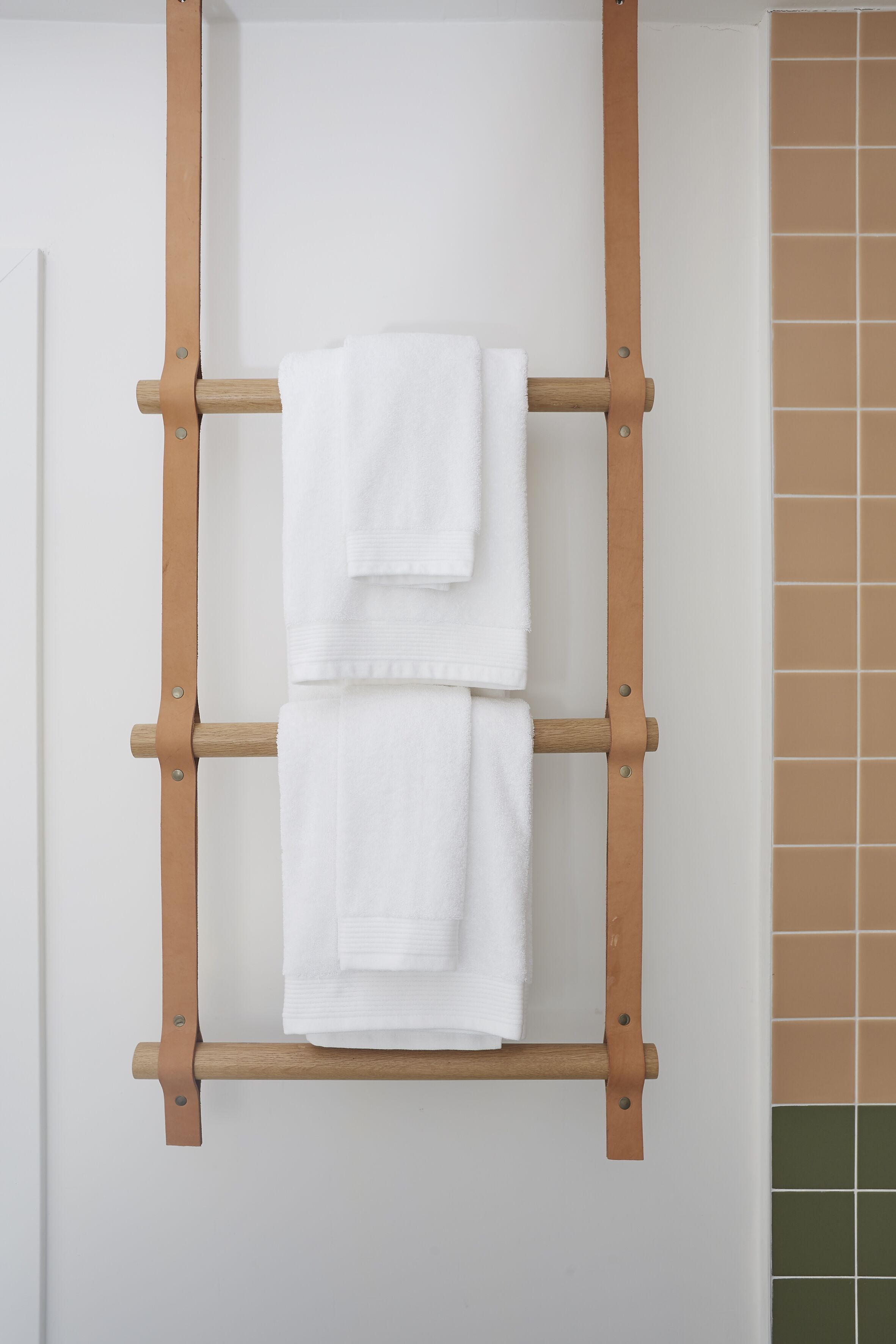 A wooden towel rack with two white towels hanging.