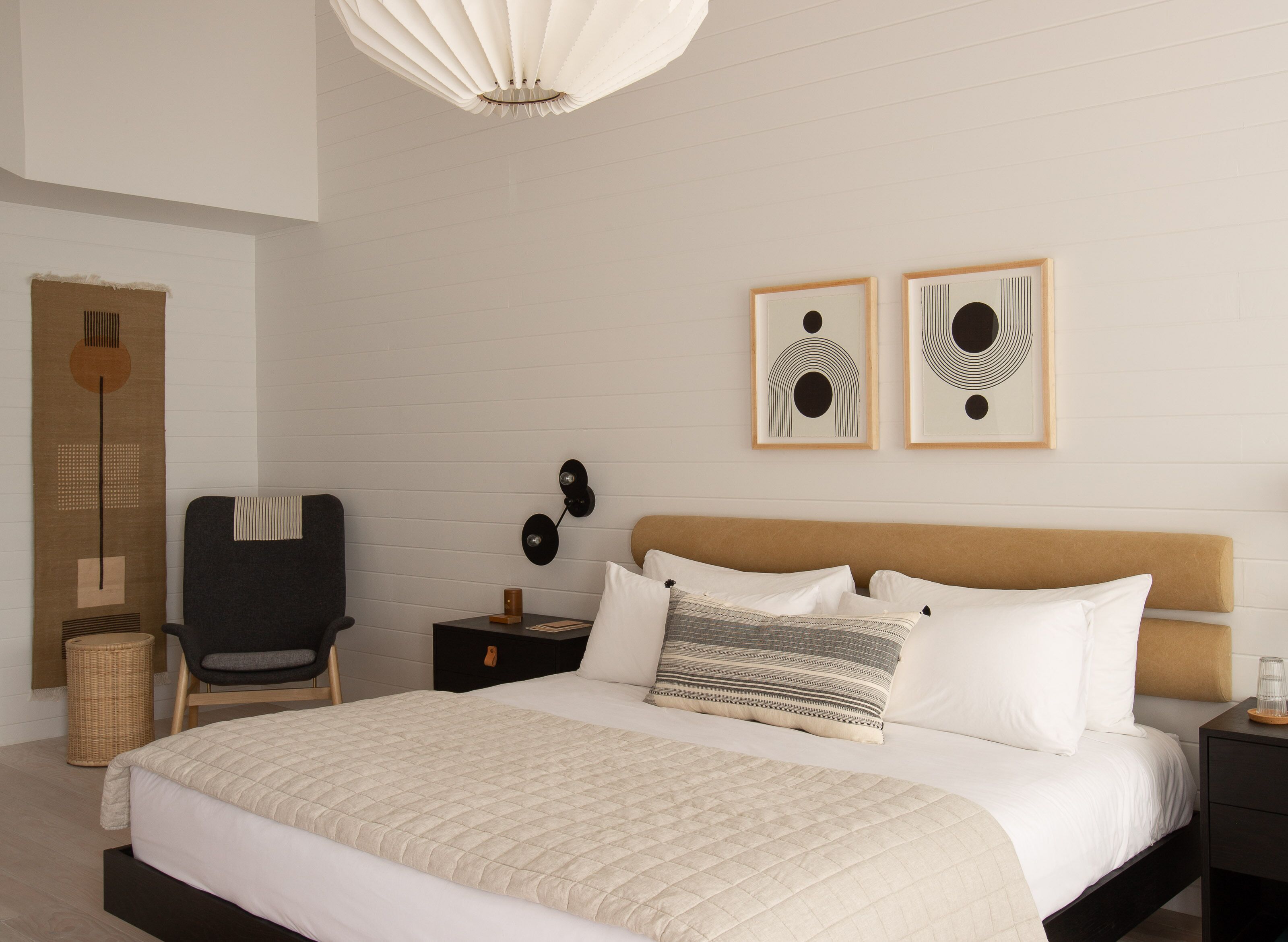 A bedroom with a bed, a chair, a nightstand, and two wall art pieces.