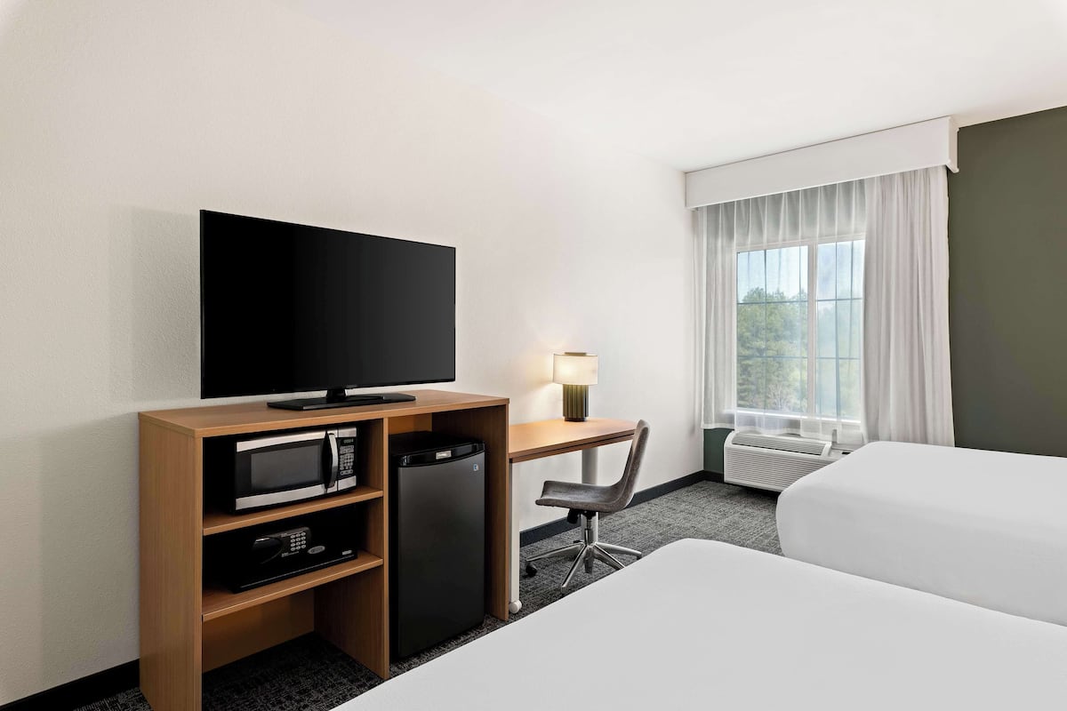 A hotel room with a TV, microwave, refrigerator, desk, chair, and a bed.