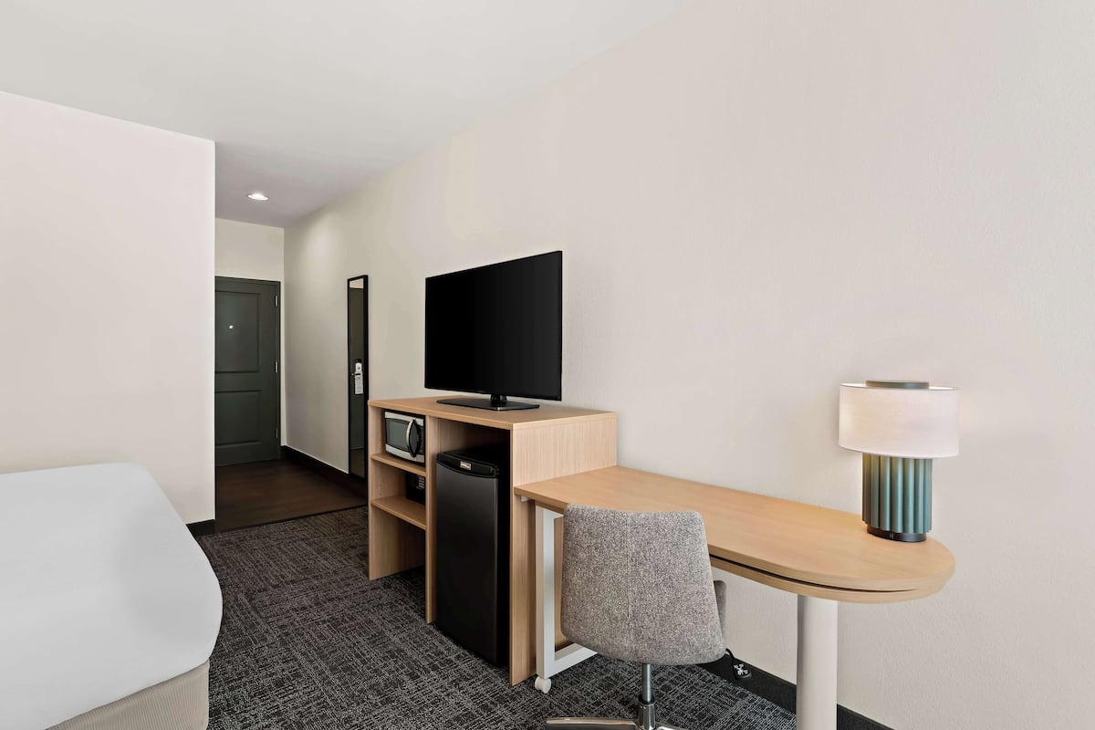 A hotel room with a wooden desk, a television, a lamp, and a grey chair.