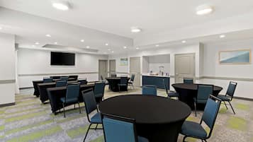 Une salle de conférence équipée de tables rondes, de chaises, d’un téléviseur à écran plat et de luminaires encastrés dans le plafond.