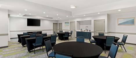 Une salle de conférence équipée de tables rondes, de chaises, d’un téléviseur à écran plat et de luminaires encastrés dans le plafond.