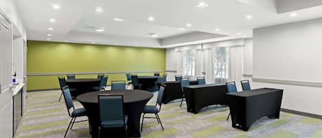 Une salle de conférence équipée de tables rondes, de chaises et d’un écran de projection.