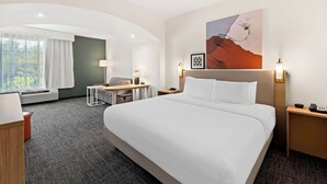 A hotel room with a large bed, a desk, a chair, a lamp, and a painting on the wall.